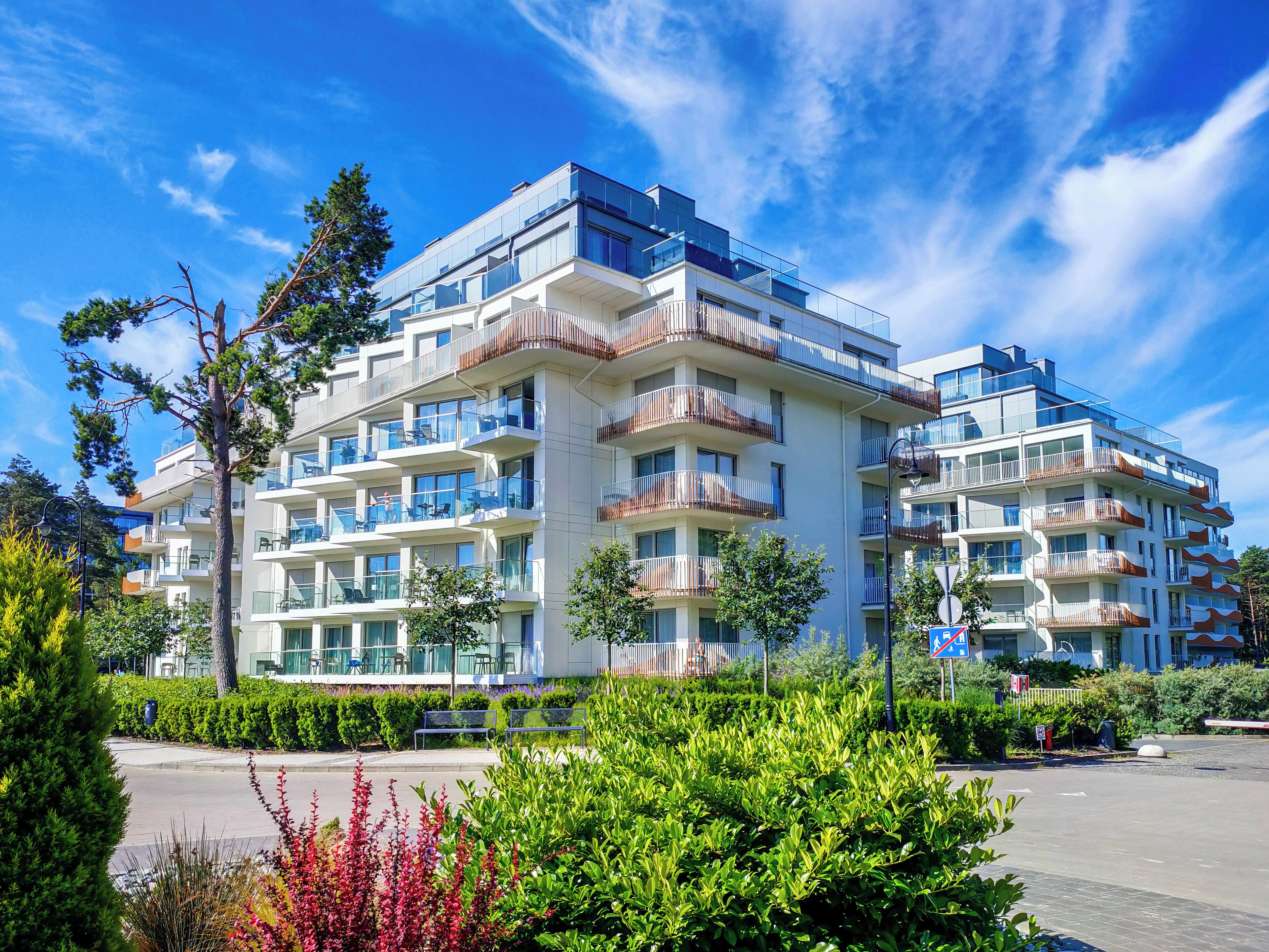 A modern multi-story residential building with balconies, a parking area, and well-maintained greenery.