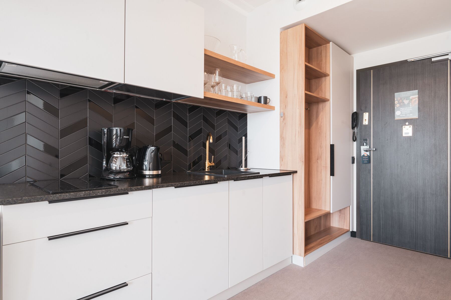 Eine moderne Küche mit schwarzem Fischschuppen-Spritzschutz, weißen Schränken und einem Holzregal über der Arbeitsplatte.