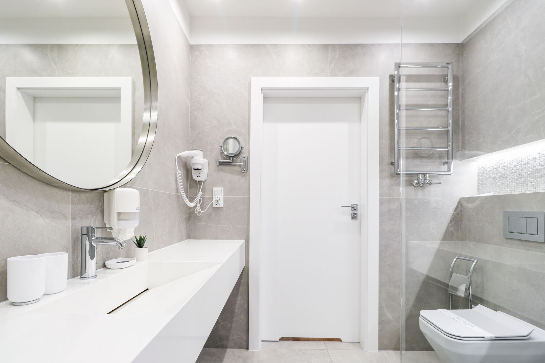 A modern bathroom with a white sink, a mirror, a hairdryer, and a toilet.