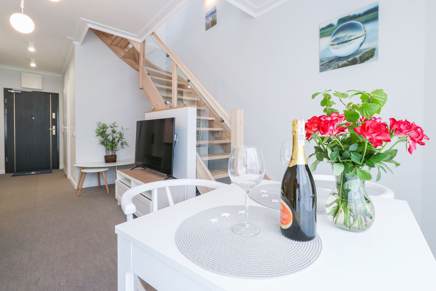 Una habitación moderna con una mesa blanca, una botella de champán y un jarrón de flores rojas.