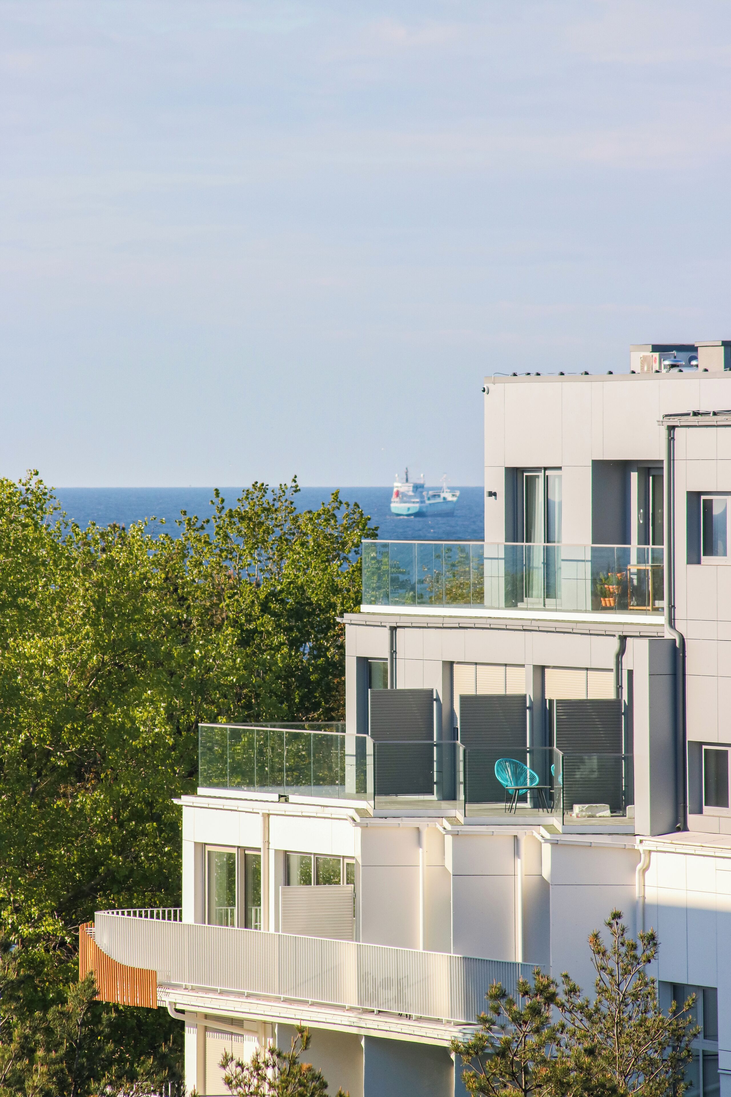 A modern multi-story building with balconies, large windows, and a view of the sea.