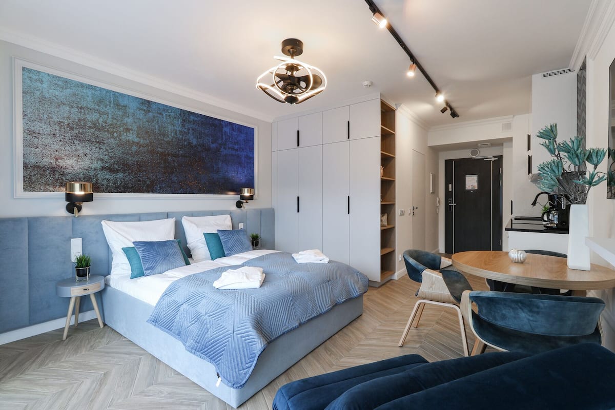 Ein modernes Schlafzimmer mit einem großen Bett, Nachttischen, einem Schreibtisch und einem Stuhl. Ein Kleiderschrank und eine Tür zum Badezimmer sind ebenfalls vorhanden.