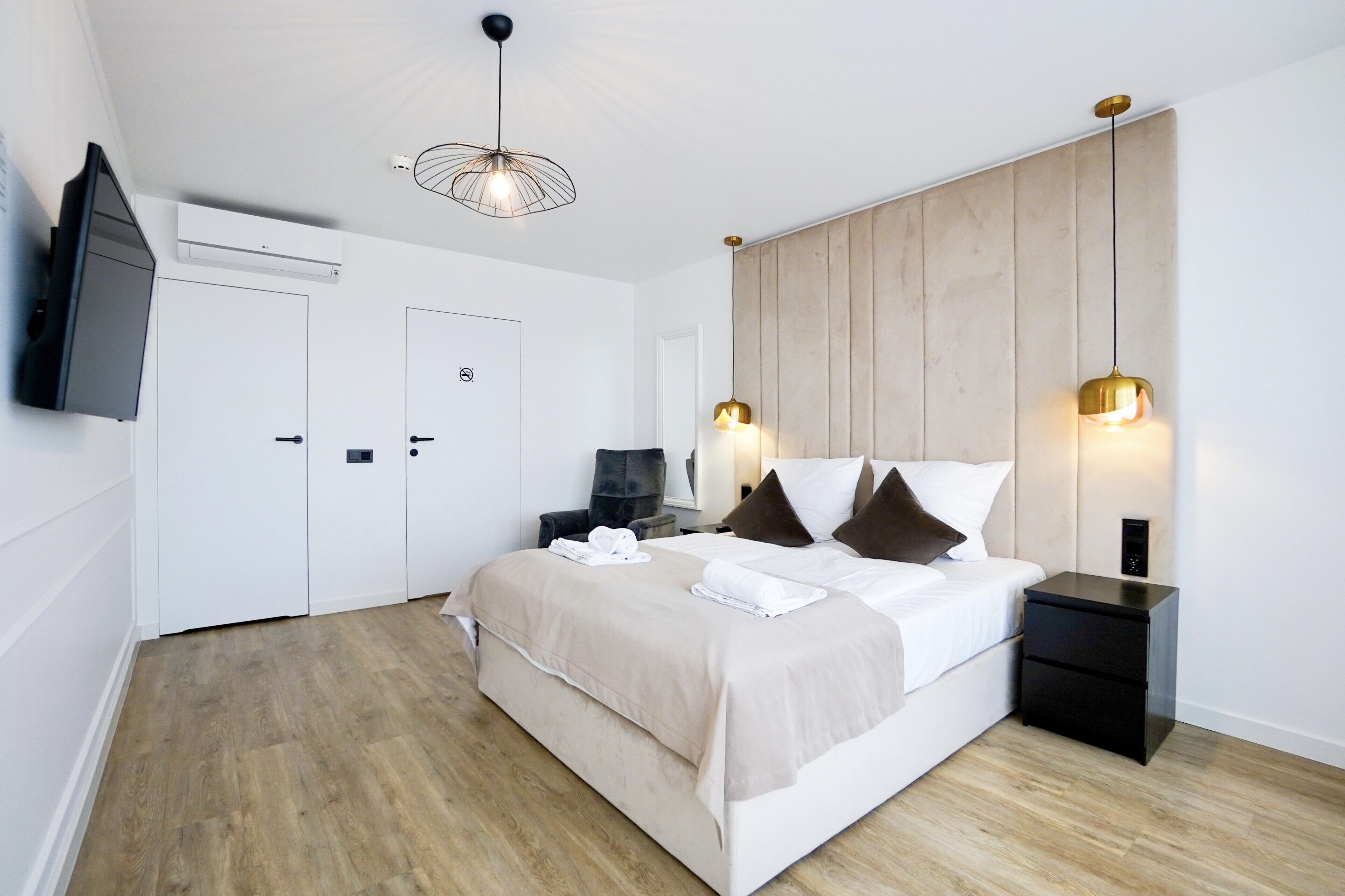 A modern hotel room with a large bed, two bedside tables, a TV mounted on the wall, and a wooden panel wall.