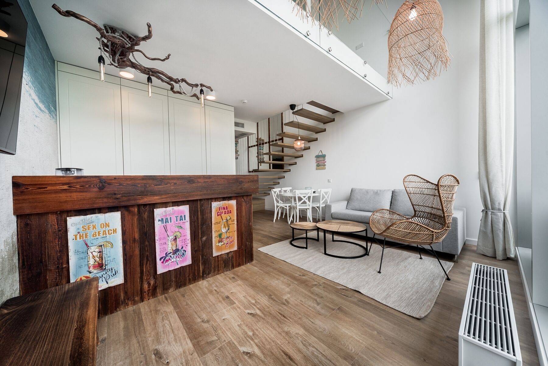 Un intérieur moderne avec un comptoir d’accueil en bois, des chaises blanches, un canapé gris et un escalier.