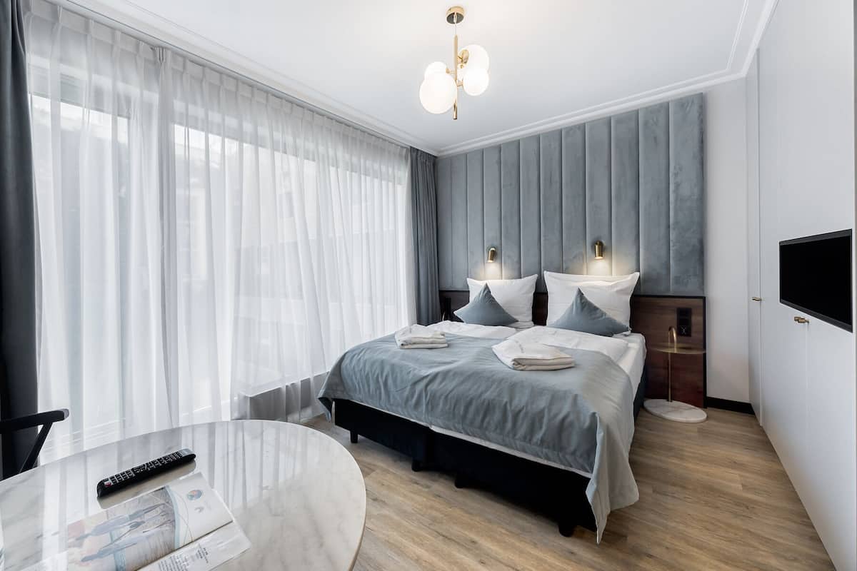 Ein modernes Hotelzimmer mit einem großen Bett, Nachttischlampen, einem Fernseher und einem runden Tisch mit Fernbedienung.