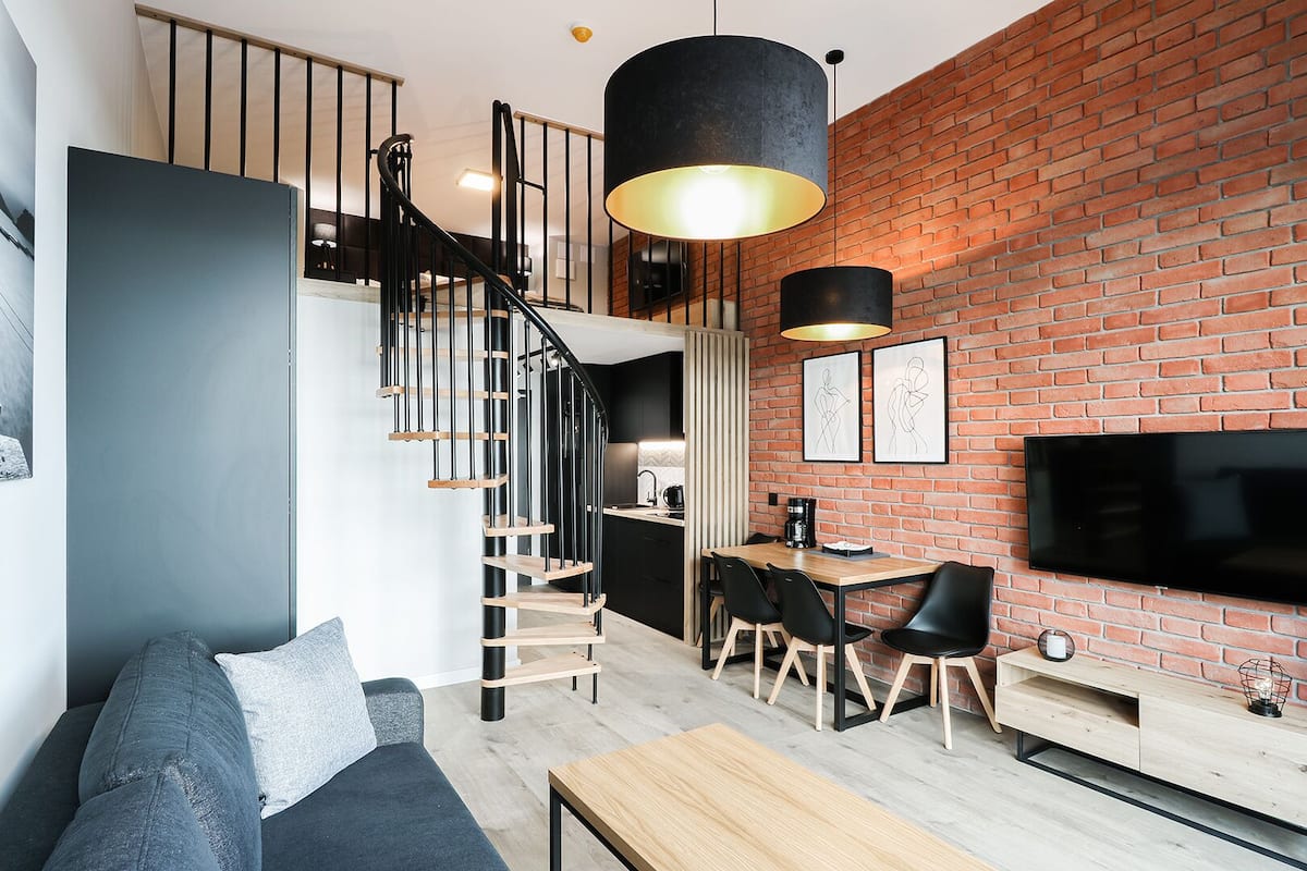 Ein moderner Wohnraum mit Treppe, Essbereich und einem an einer Ziegelwand montierten Flachbildfernseher.