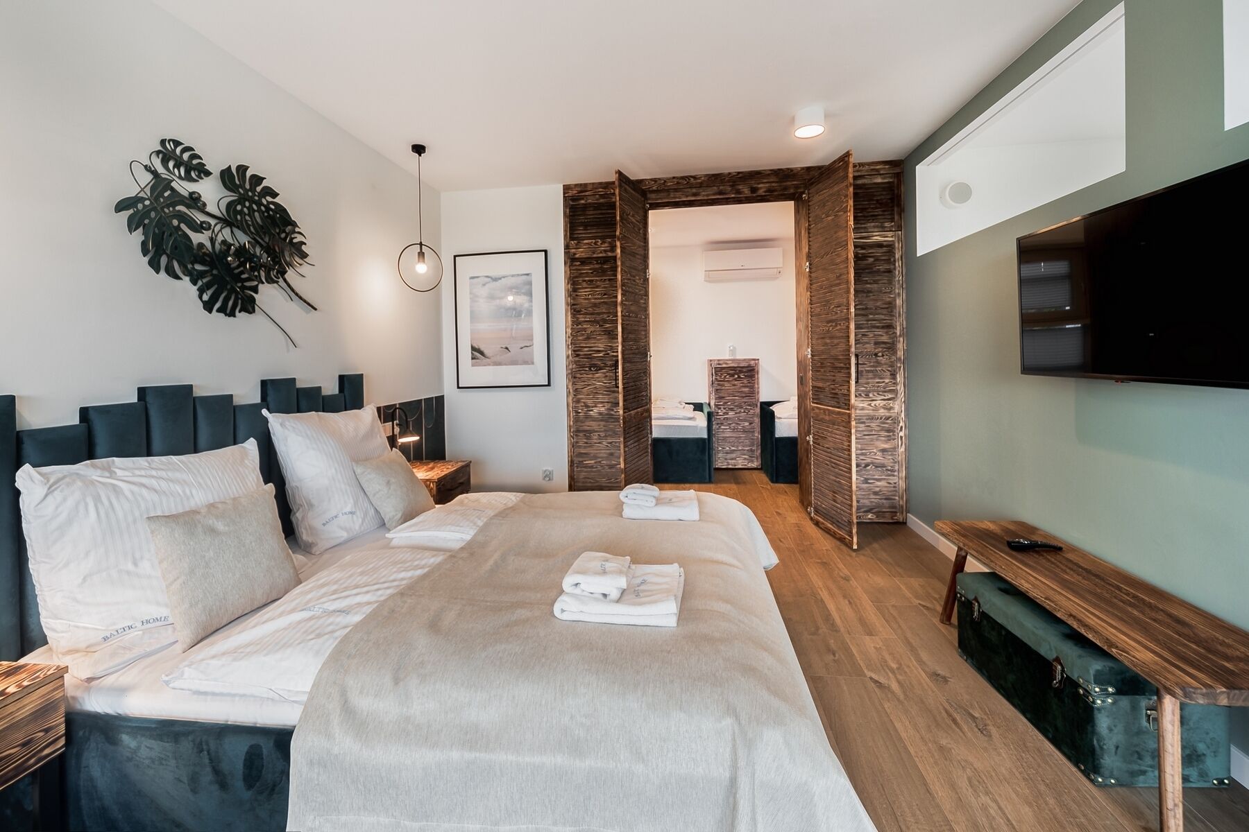 A modern hotel room with a large bed, a desk, a TV, and a plant.
