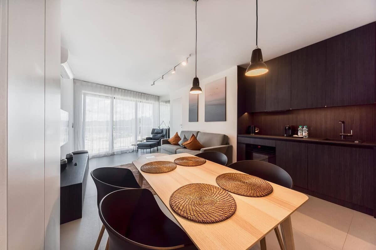 Eine moderne Küche mit dunklen Holzschränken, einem Holzesstisch mit gewebten Platzsets und Pendelleuchten.