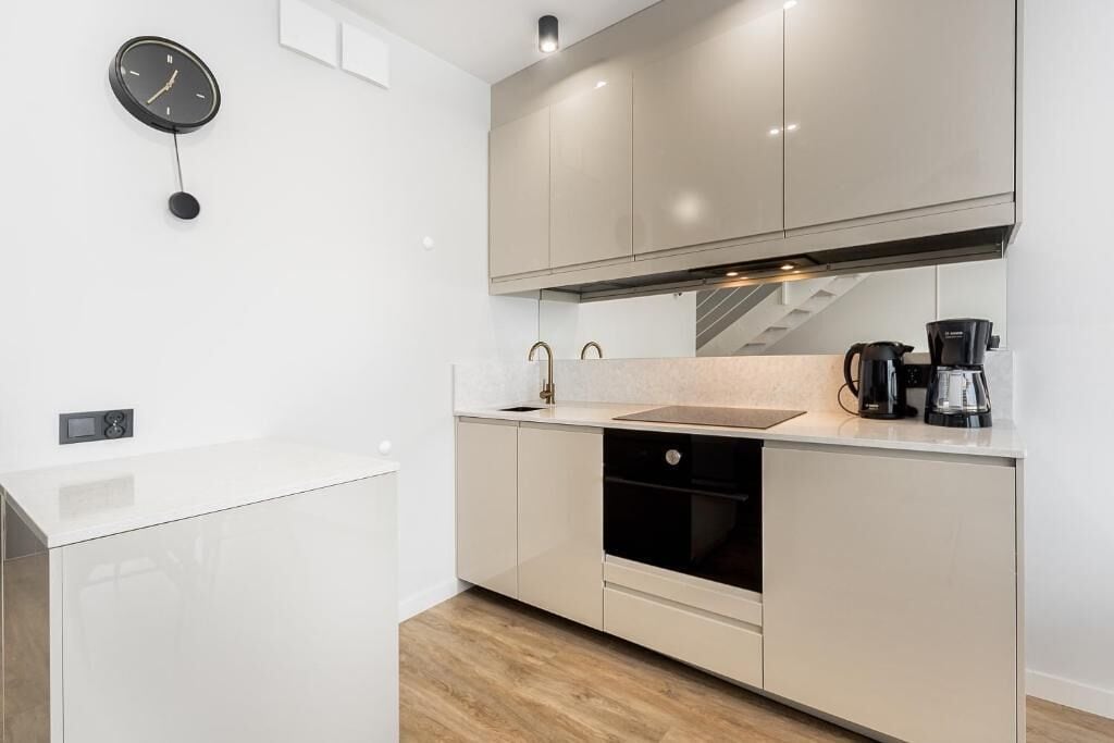 A modern kitchen with a sink, stove, and a clock on the wall.