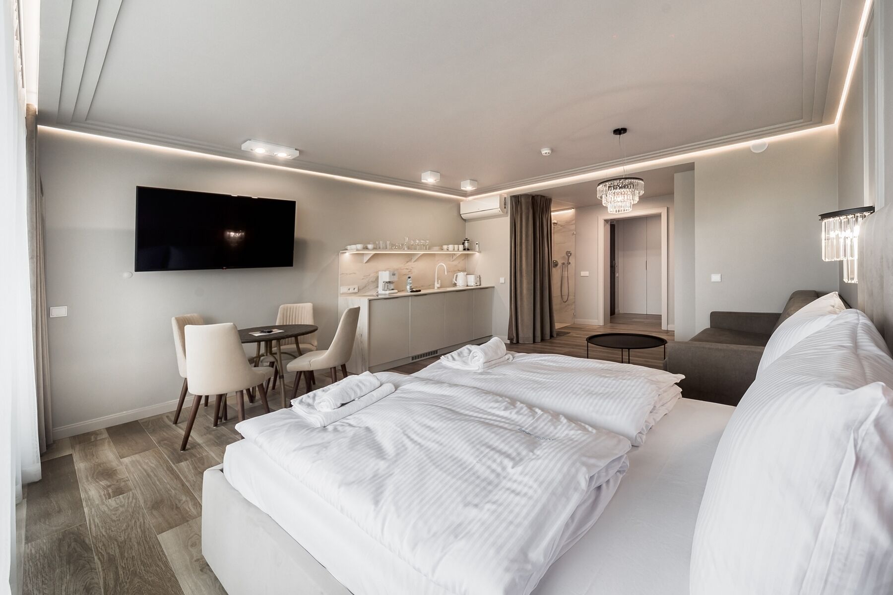 Ein modernes Hotelzimmer mit einem großen Bett, einem an der Wand montierten Fernseher, einer kleinen Essecke und einem separaten Badezimmer.