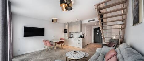 A modern living room with a grey sofa, a coffee table, and a dining area with a white table and pink chairs.