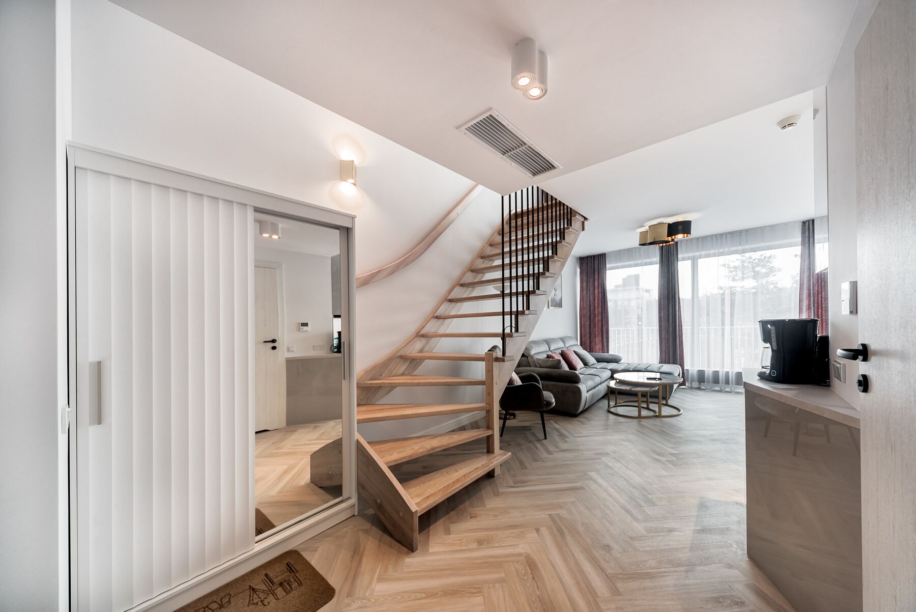 A modern interior with a wooden staircase, a living area with a sofa and coffee table, and a kitchen area.