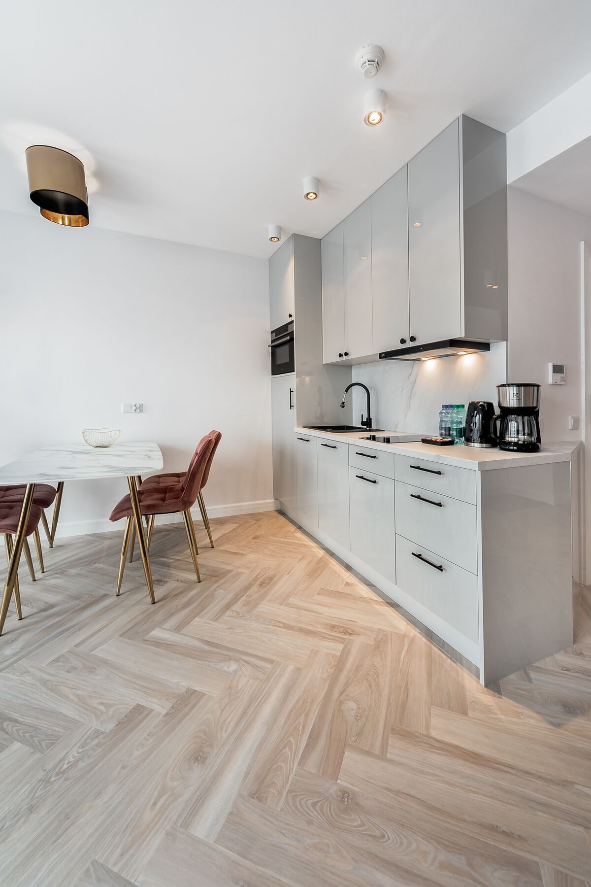 A modern kitchen with white cabinets, a marble countertop, and a herringbone wood floor.