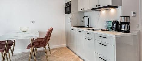 A modern kitchen with white cabinets, a marble countertop, and a herringbone wood floor.