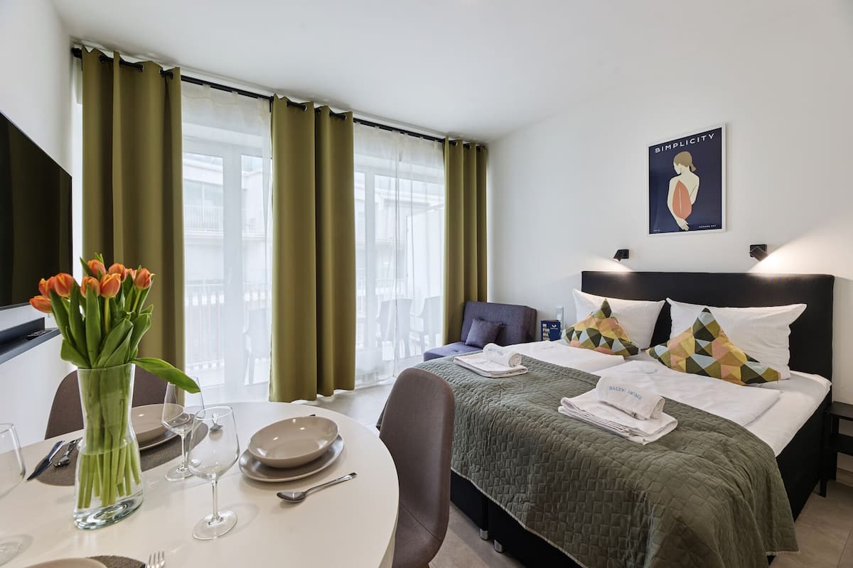 Ein Hotelzimmer mit einem Bett, einem Esstisch mit einer Tulpenvase und einem Gemälde an der Wand.