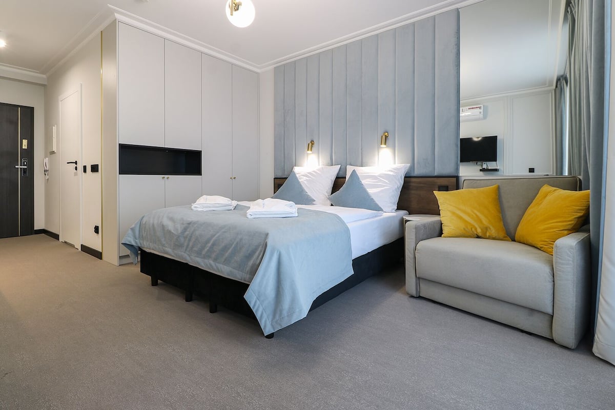 Ein modernes Schlafzimmer mit einem Bett, Nachttischen, einem Sofa und einem großen Spiegel.