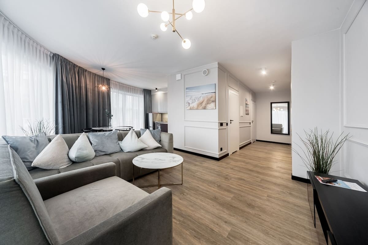 Ein modernes Wohnzimmer mit einer grauen Couch, einem runden Couchtisch und einem Essbereich mit Tisch und Stühlen.
