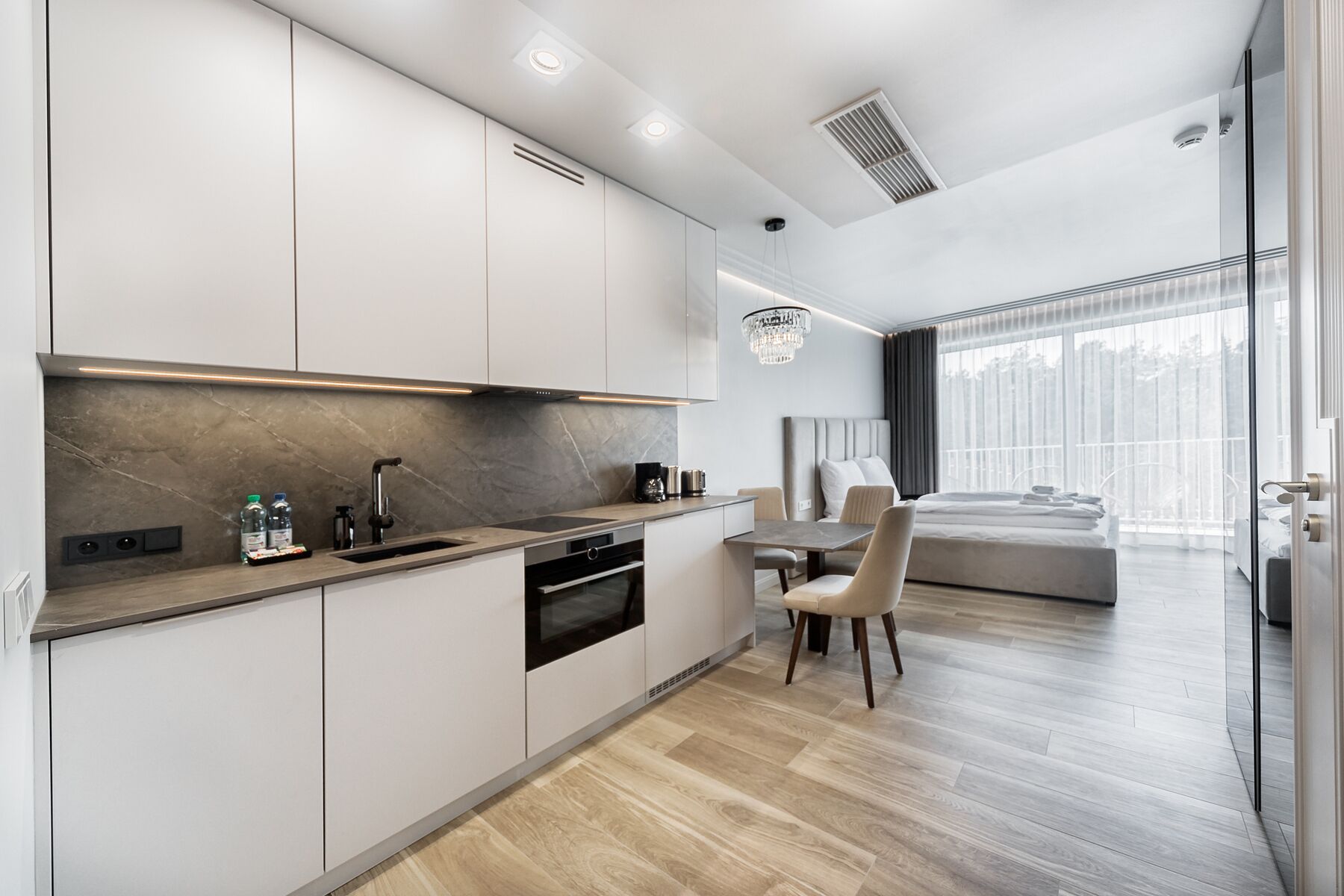 A modern kitchen with a dining area, a built-in oven, and a large window overlooking a balcony.