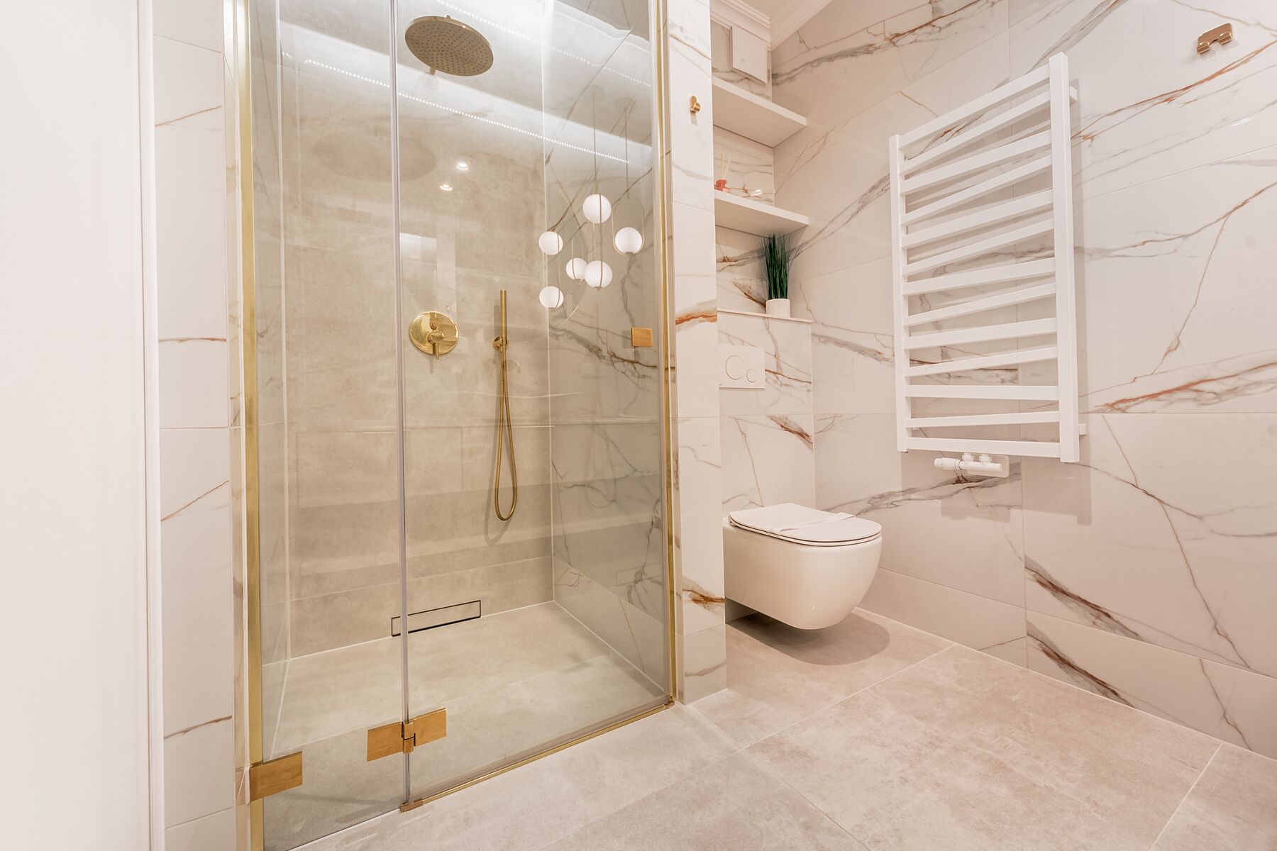 Ein modernes Badezimmer mit einer gläsernen Duschkabine, einer weißen Toilette und einer Wand mit Marmorfliesen.
