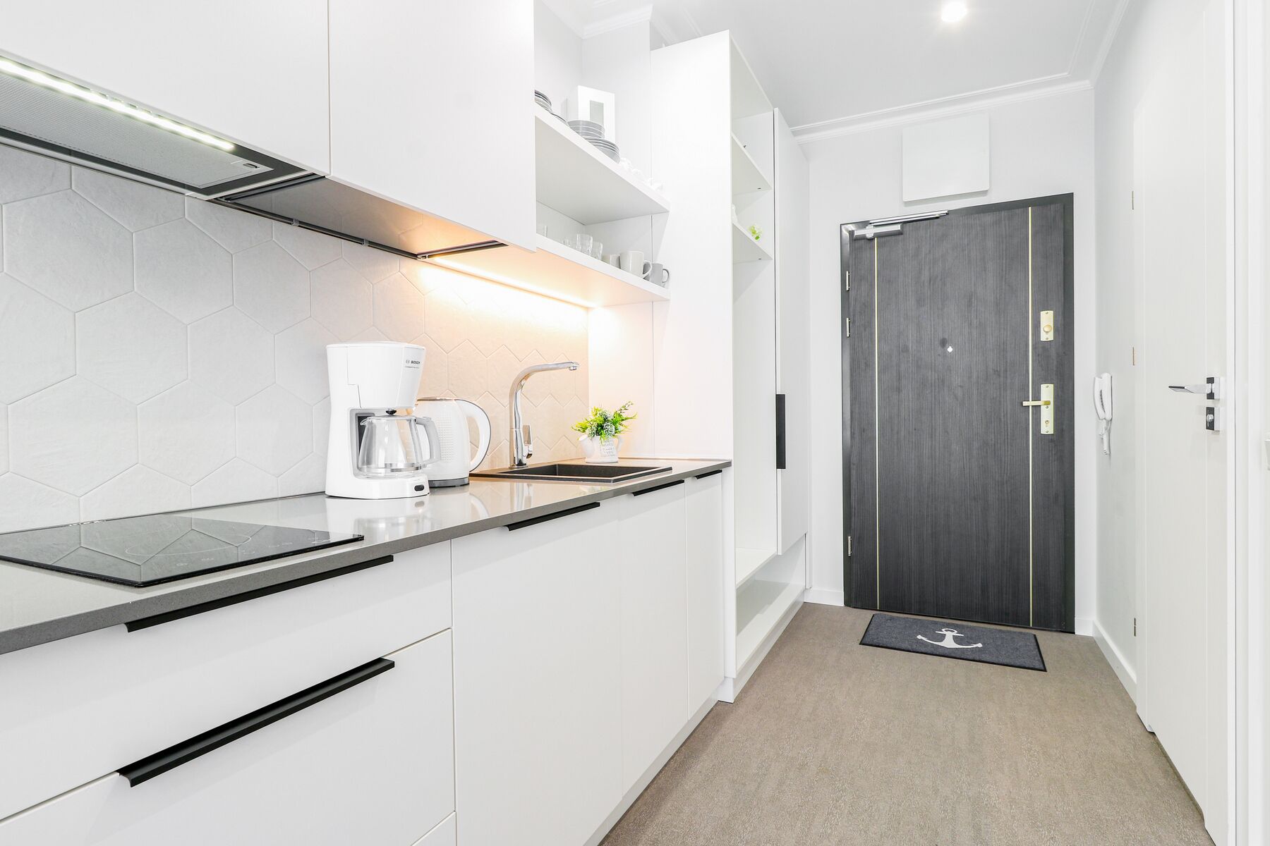 A modern kitchen with white cabinets, a Bosch coffee maker, a sink, and a dark wooden door.