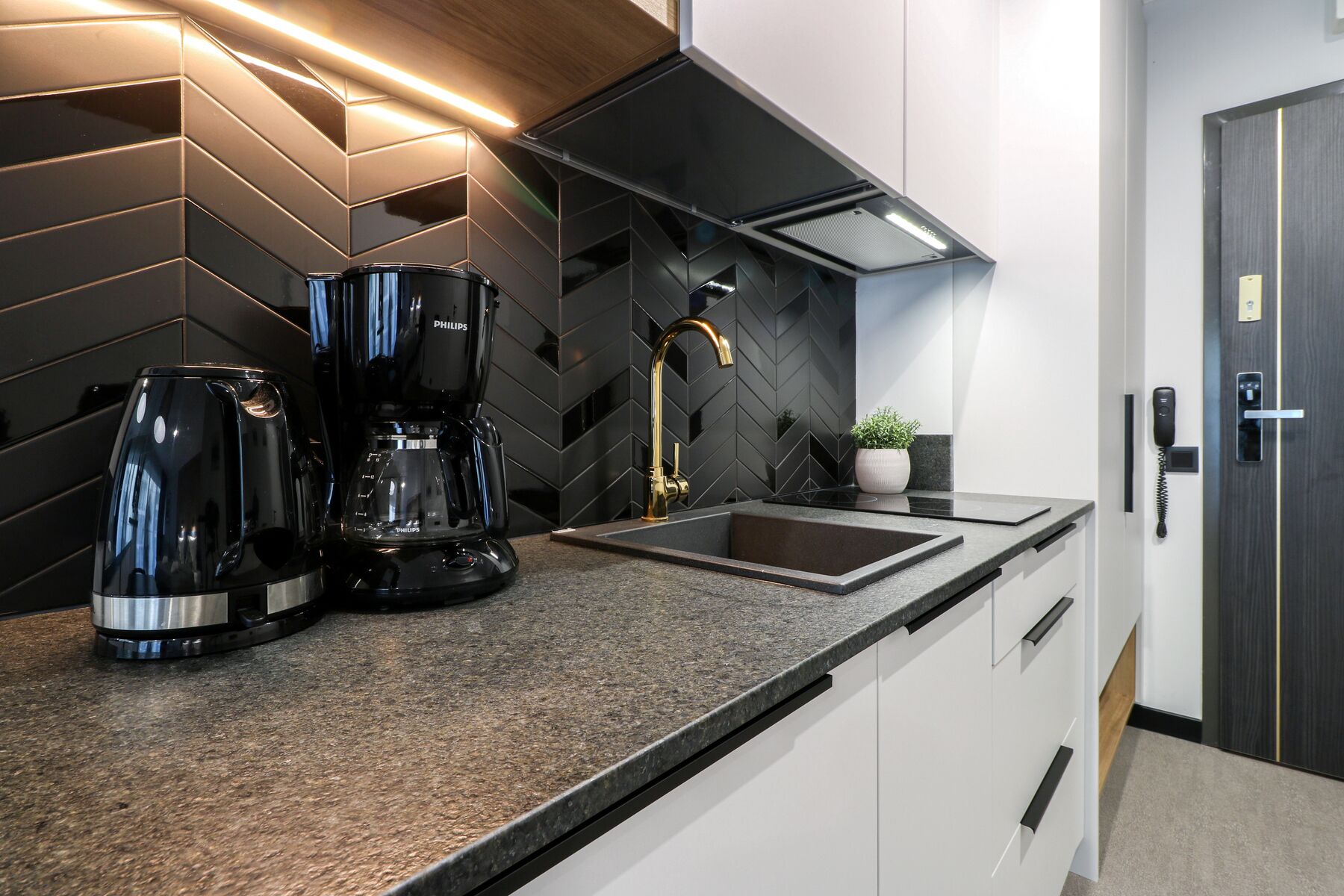 A modern kitchen with a black and white color scheme, featuring a coffee maker, a sink, and a potted plant.