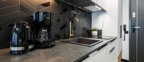 A modern kitchen with a black and white color scheme, featuring a coffee maker, a sink, and a potted plant.