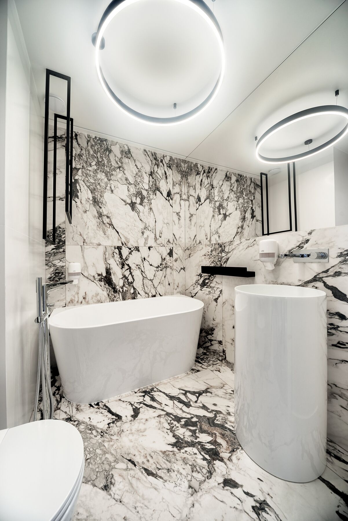 A modern bathroom with a freestanding bathtub, a round sink, and marble walls.