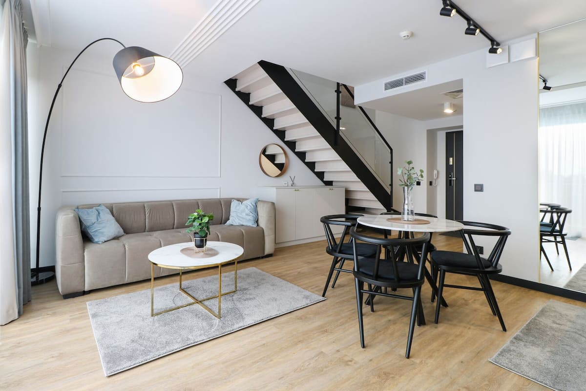 Ein modernes Wohnzimmer mit einer Couch, einem Couchtisch, Sesseln, einer Treppe und einem Essbereich mit Tisch und Stühlen.