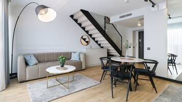 A modern living room with a sofa, coffee table, and chairs, a staircase, and a dining area with a table and chairs.