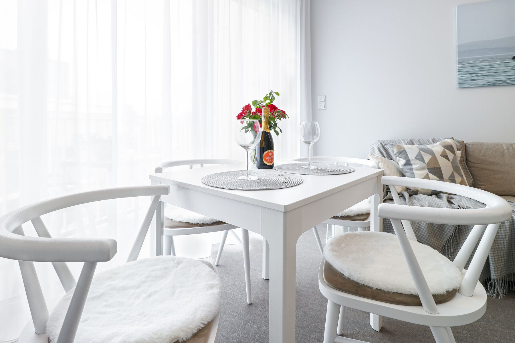A white dining table with two chairs, a bottle of champagne, and two glasses.