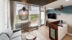 A modern living room with a large window, a sofa, a dining table, and a TV mounted on the wall. -  ApartPark by Baltic Home (Swinoujscie)