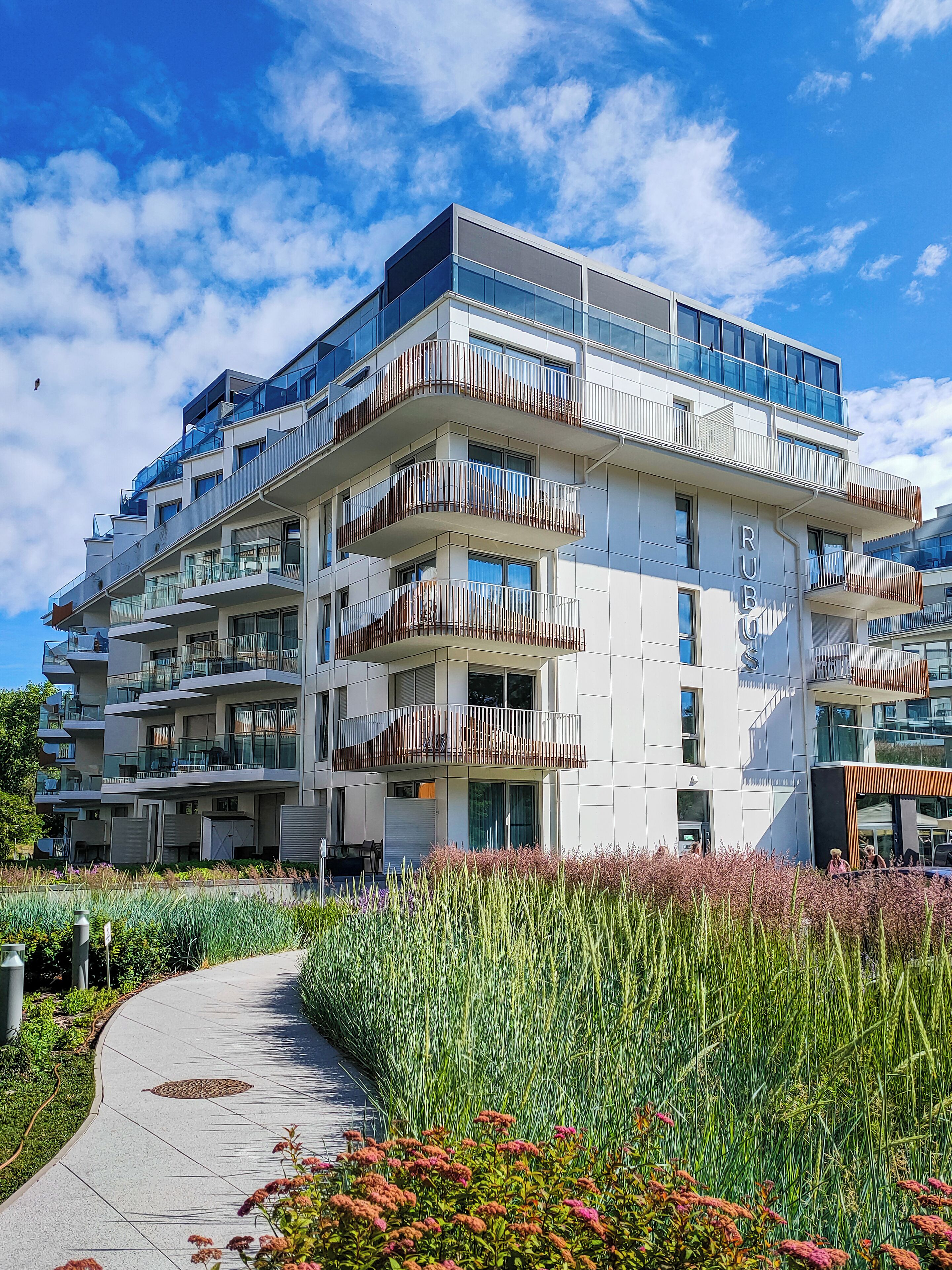 A multi-story residential building with balconies, a pathway, and a garden area.