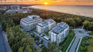 A modern residential complex with multiple buildings, a parking area, and a view of the sea at sunset. -  ApartPark by Baltic Home (Swinoujscie)