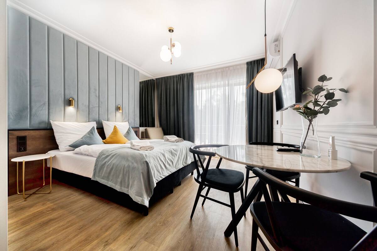 Ein modernes Hotelzimmer mit Bett, Nachttisch und rundem Esstisch mit Stühlen.