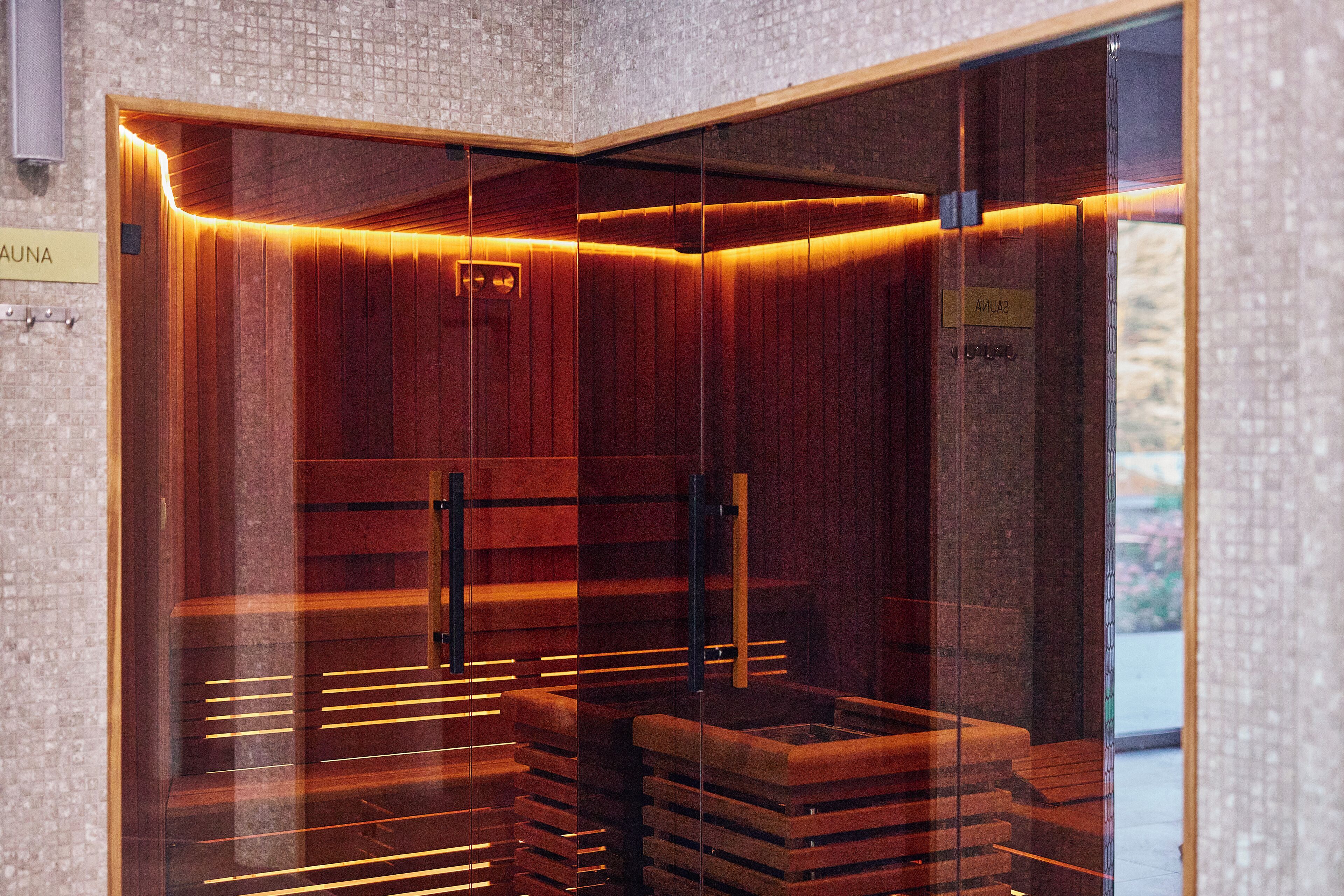 A sauna with wooden walls and a glass door, featuring a sign that reads "SAUNA".