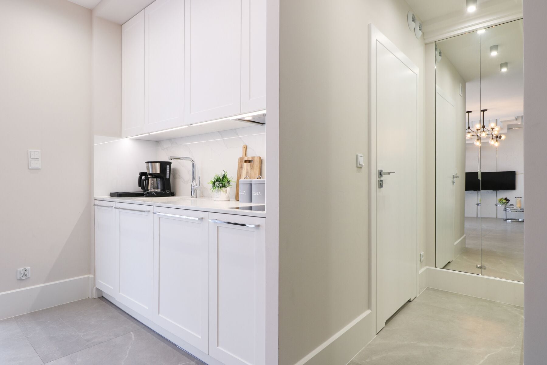 A modern kitchen with white cabinetry, a coffee maker, and a small plant.