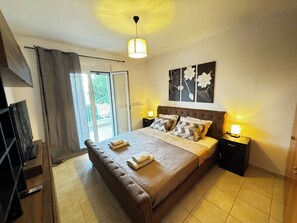 A bedroom with a large bed, two bedside tables with lamps, a ceiling light, a sliding glass door, and a view of greenery outside. - Skiathos Center Stylish 2 Bd w Balcony (Skiathos)