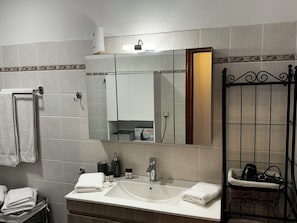 Un bagno con un lavandino bianco, uno specchio e un porta asciugamani.