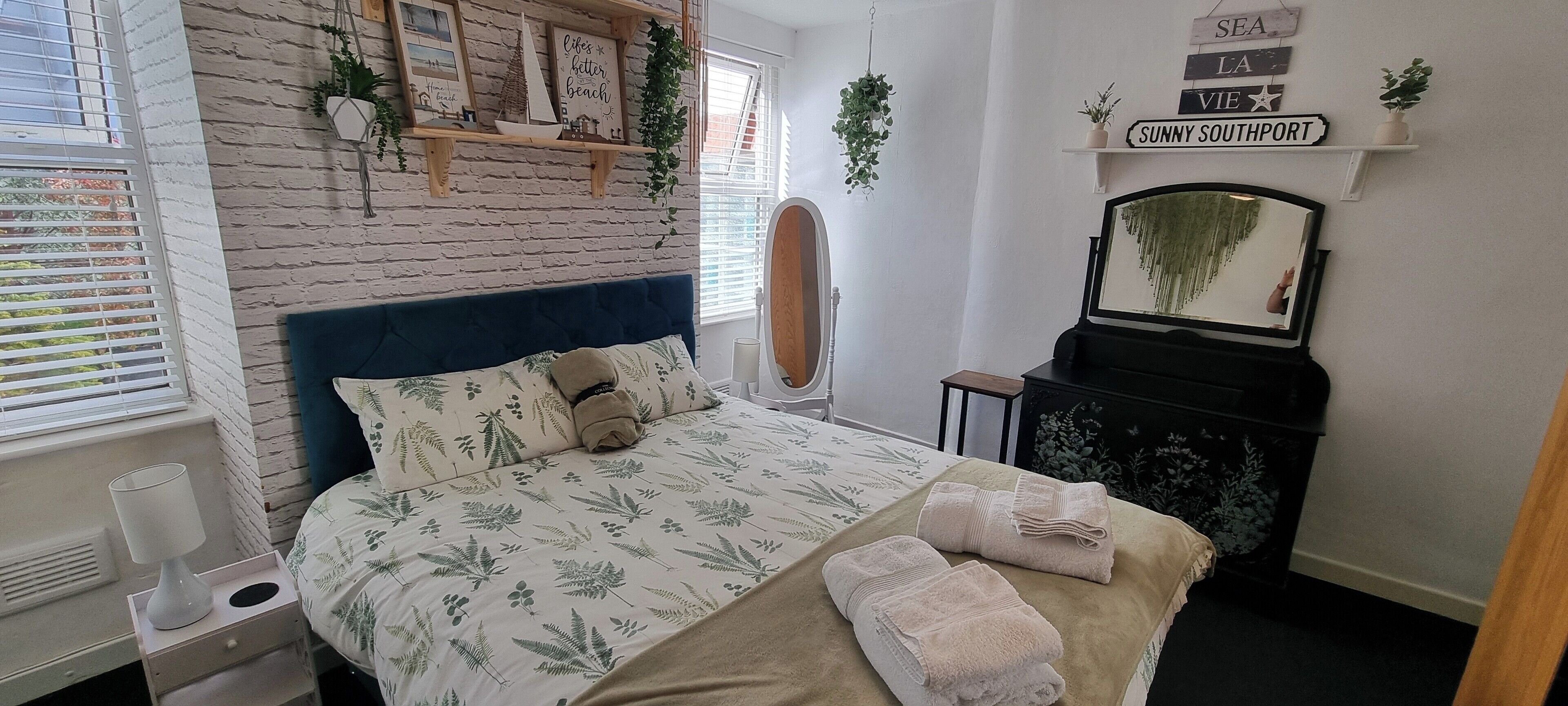 Een slaapkamer met een bed, een dressoir, een spiegel en een raam met jaloezieën.