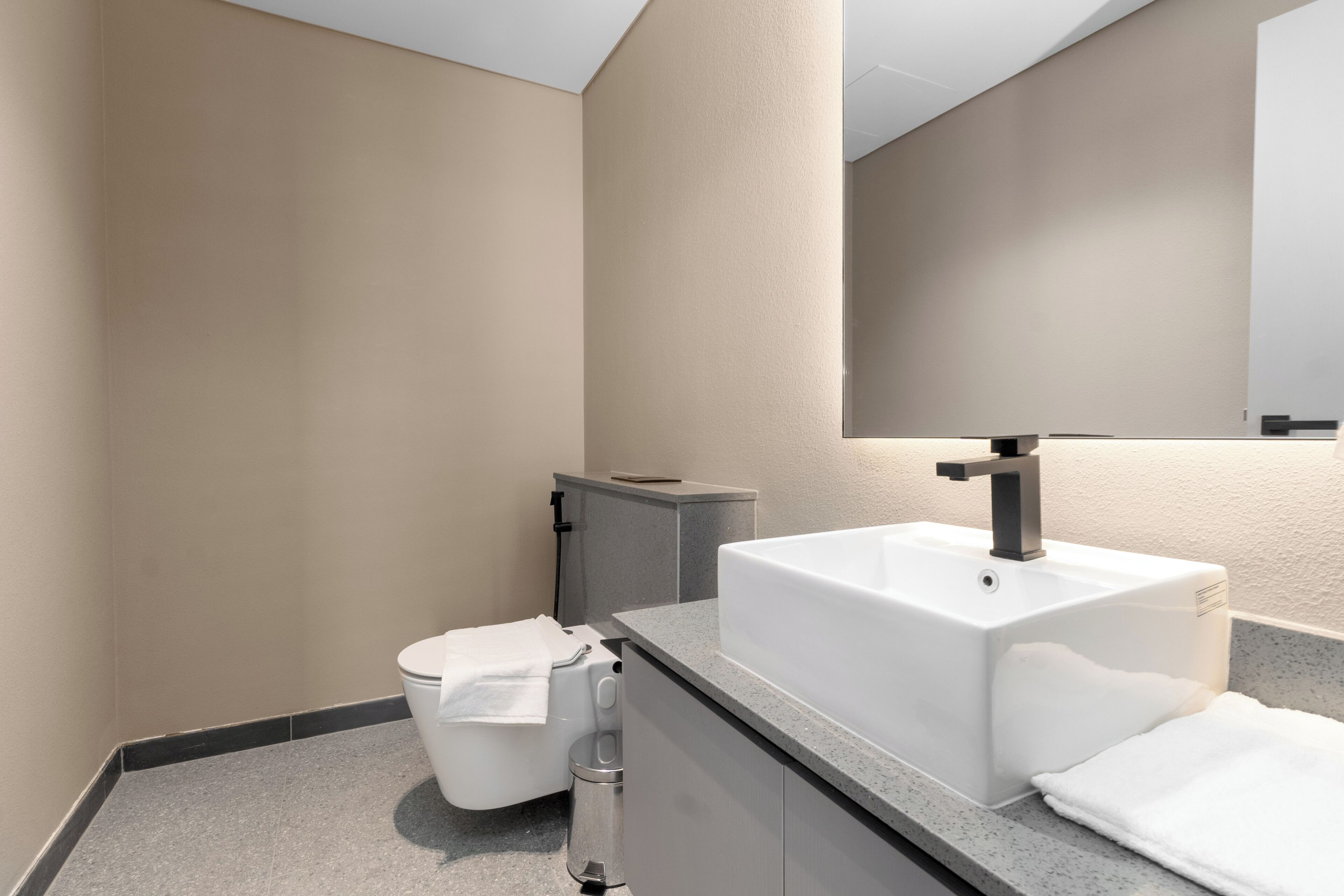 Een moderne badkamer met een wit wastafel, toilet en een prullenbak.