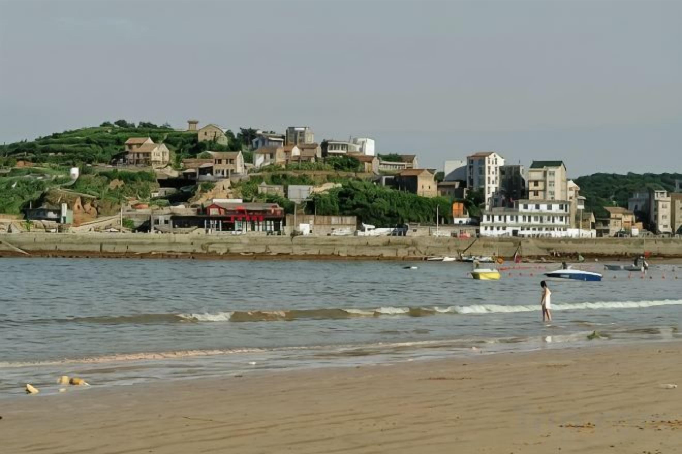 A coastal town with buildings on a hillside, a beach, and boats on the water.