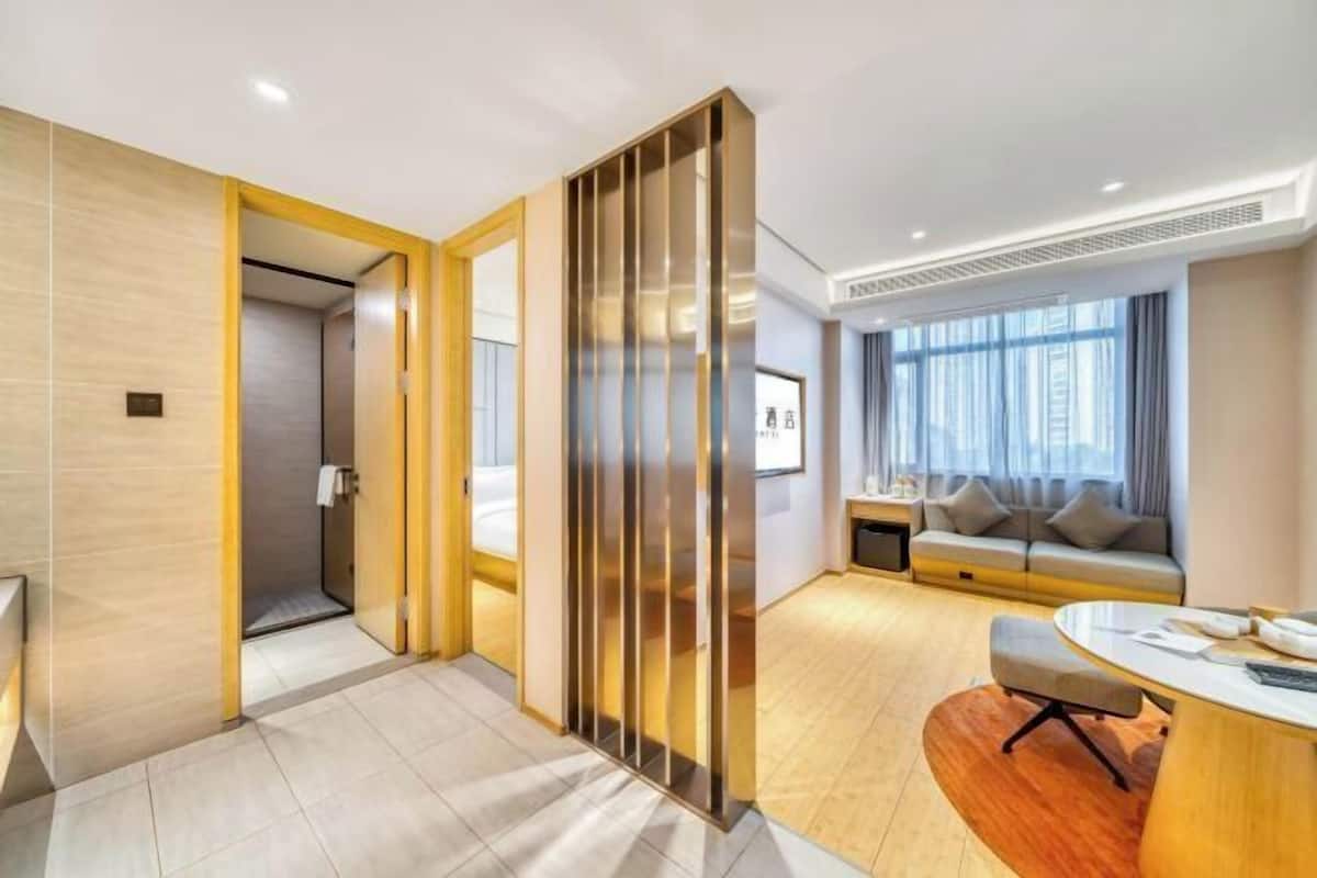 Een moderne hotelkamer met een houten vloer, een bank, een bureau en een groot raam.