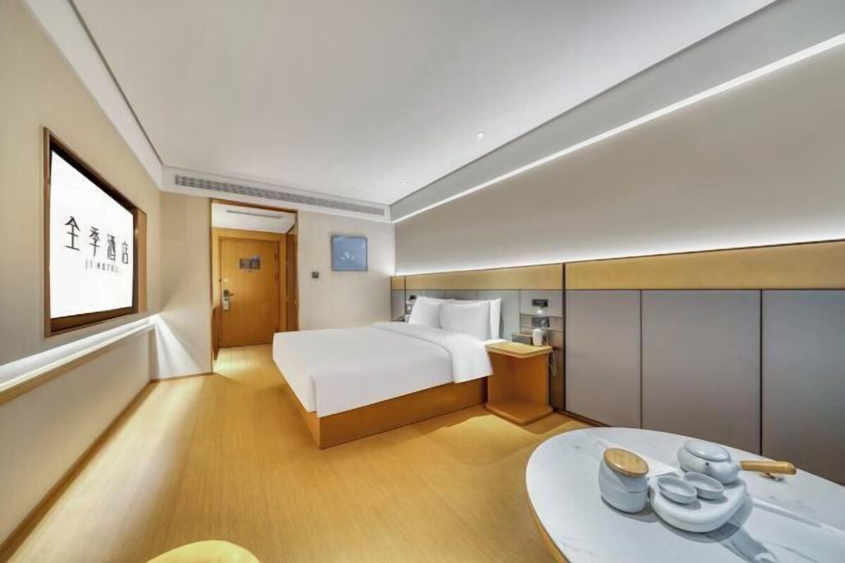A modern hotel room with a large bed, bedside table, and a small seating area with a table and stools.