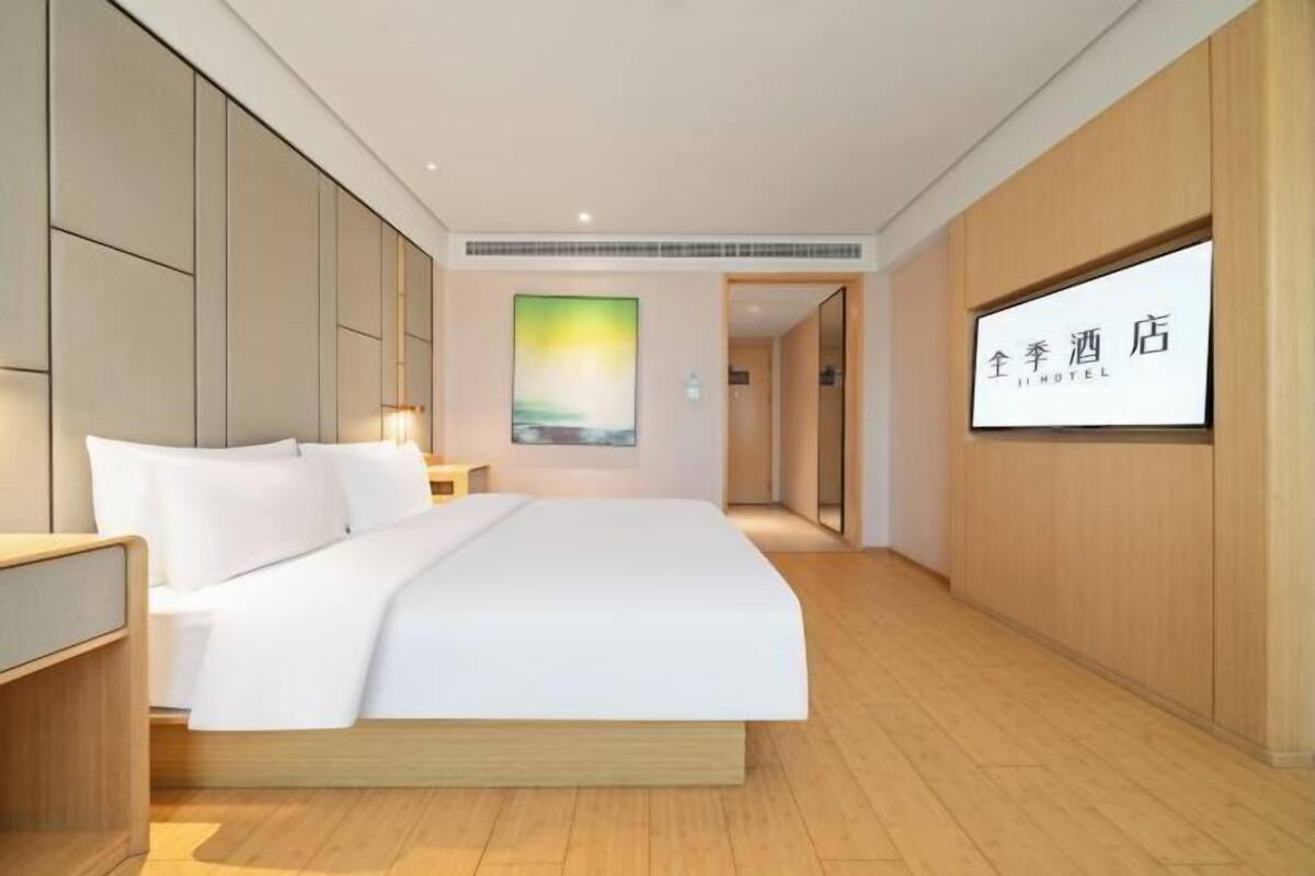 Een moderne hotelkamer met een groot bed, houten lambrisering, een flatscreen televisie en een schilderij aan de muur.