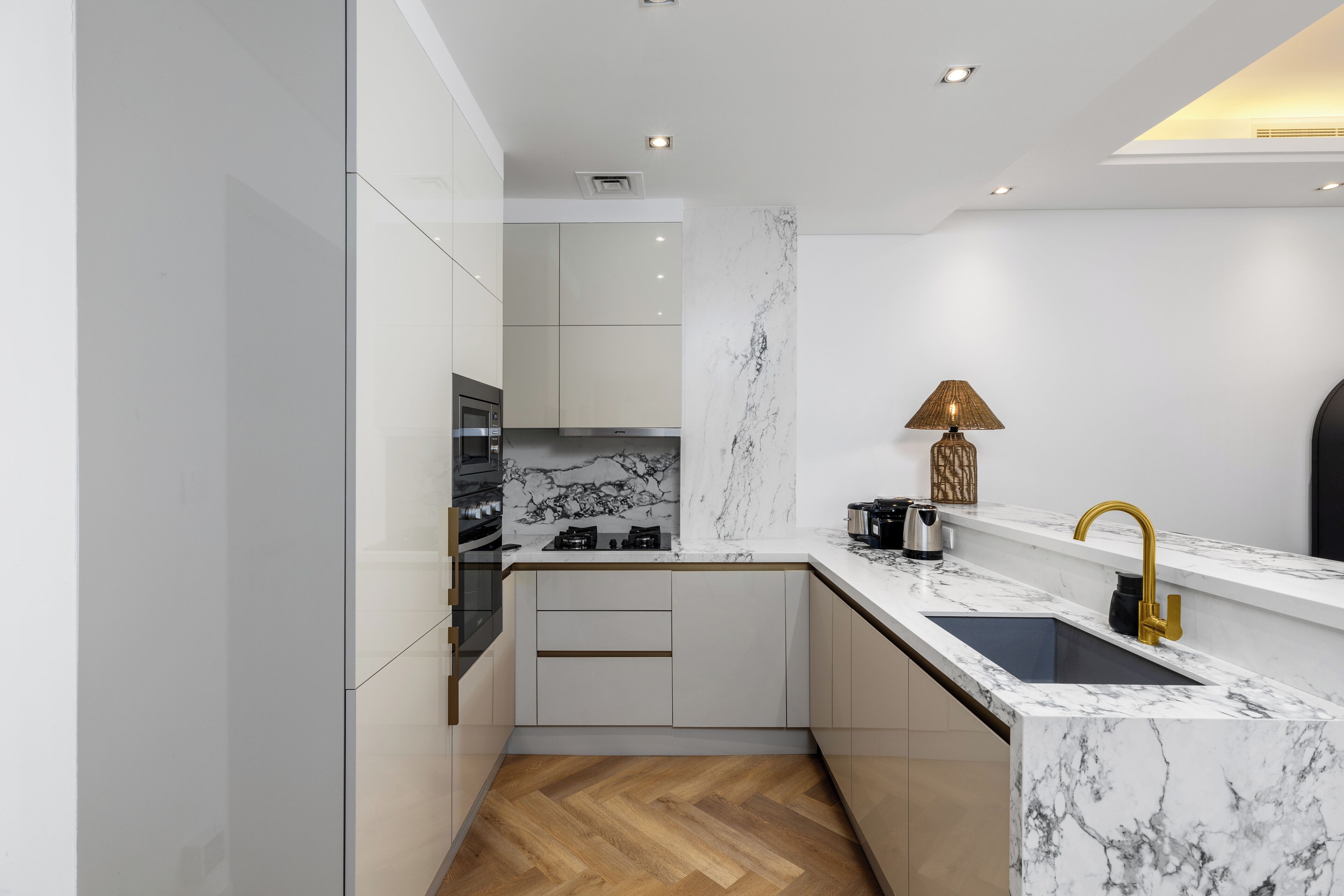 A modern kitchen with white cabinetry, a marble countertop, and a gold faucet.