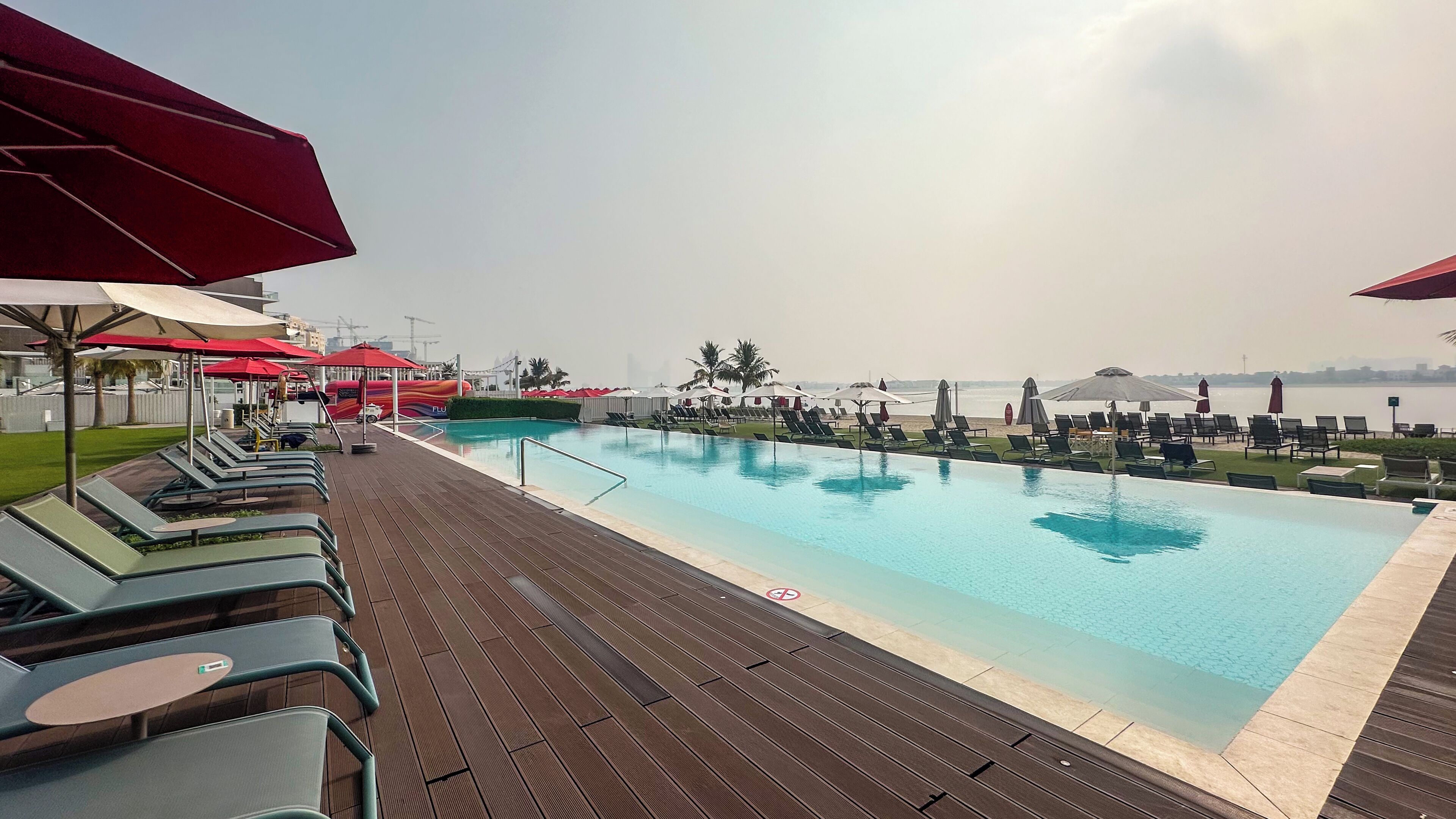 A poolside area with lounge chairs and umbrellas, a clear pool, and a view of the water and distant buildings.