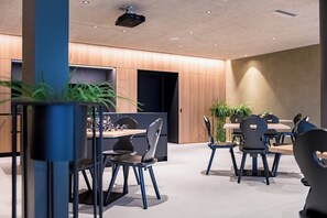 A modern conference room with a projector, tables, chairs, and potted plants.