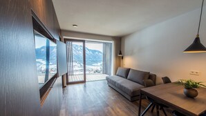 Un salon moderne avec un plancher en bois, un canapé, une table à manger et une vue sur les montagnes grâce à de grandes fenêtres.