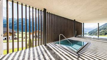 Ein Wellnessbereich mit Pool, Holzlatten und Bergblick.