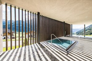 A spa area with a pool, wooden slats, and a view of mountains.